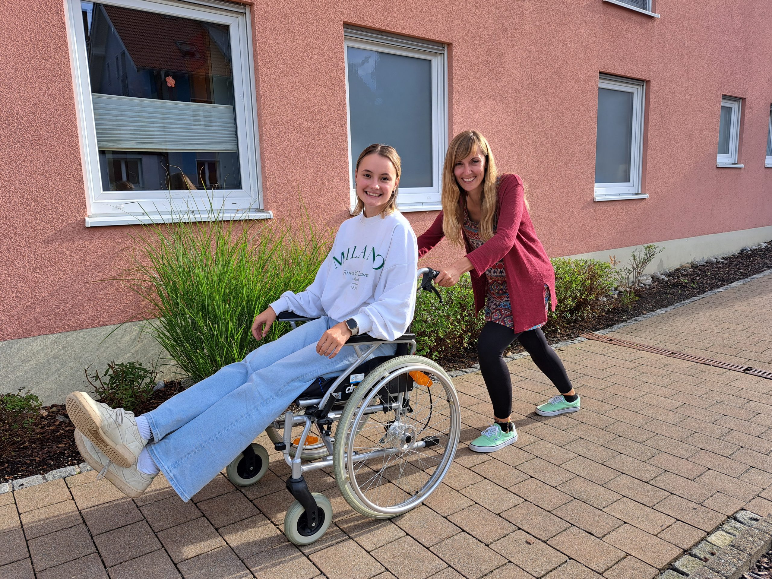 Julia schiebt Luisa im Rahmen eines Rolli-Trainings im Rollstuhl